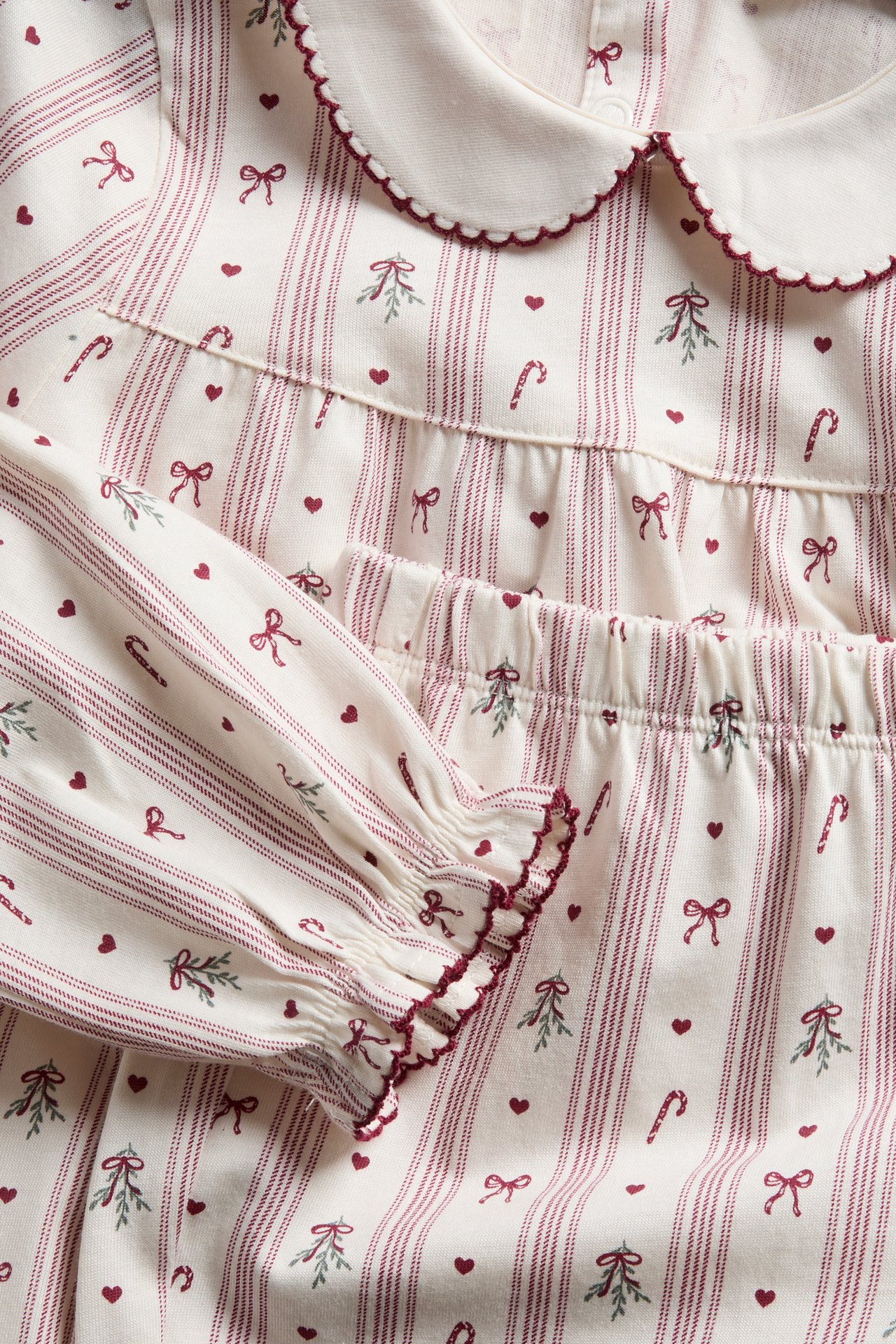 Close-up of a kid's cream pajama set with red stripes, scalloped collar, and Christmas print.