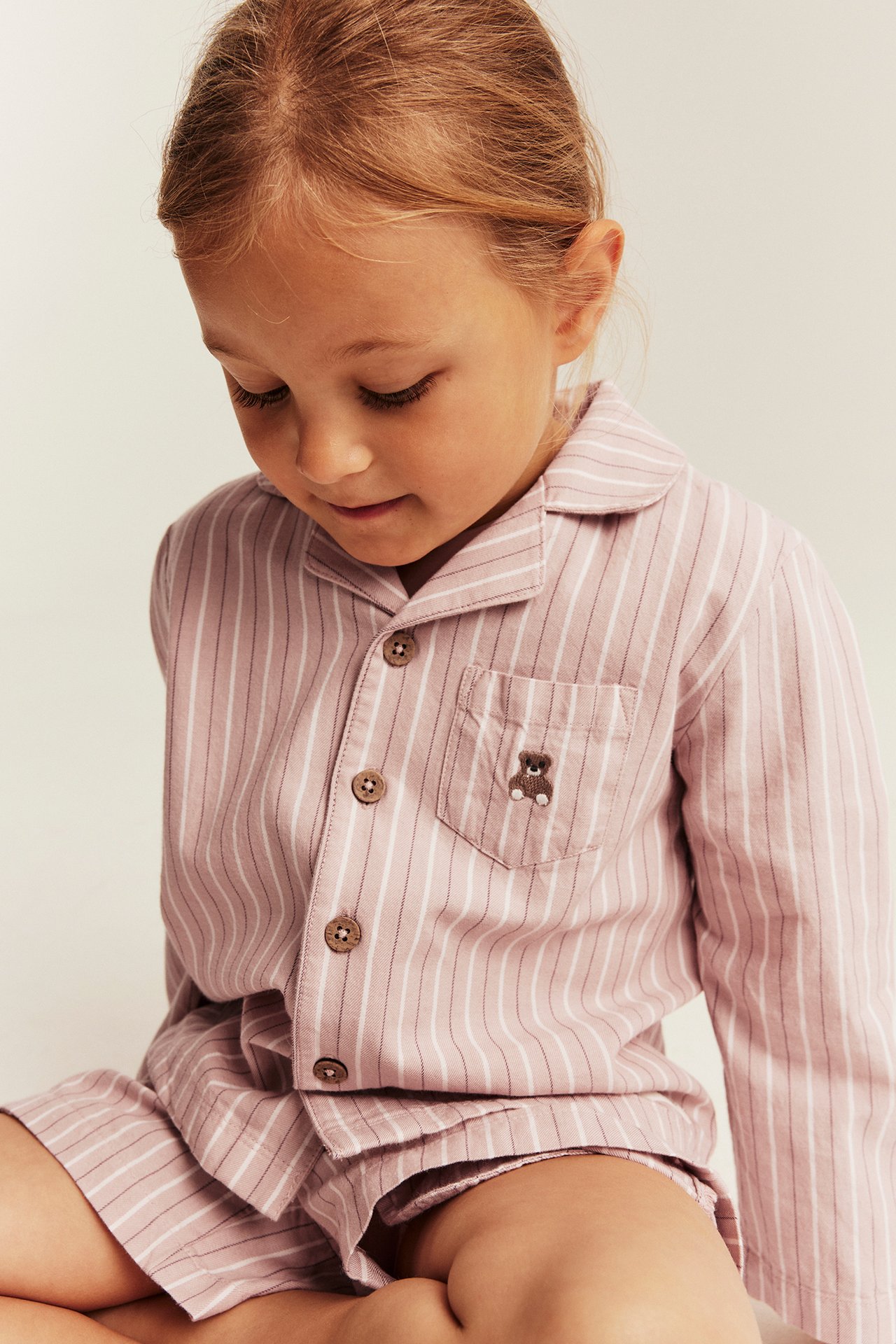 Nahaufnahme Kind in rosa gestreiftem Pyjamahemd und Shorts mit Teddybär-Stickerei.