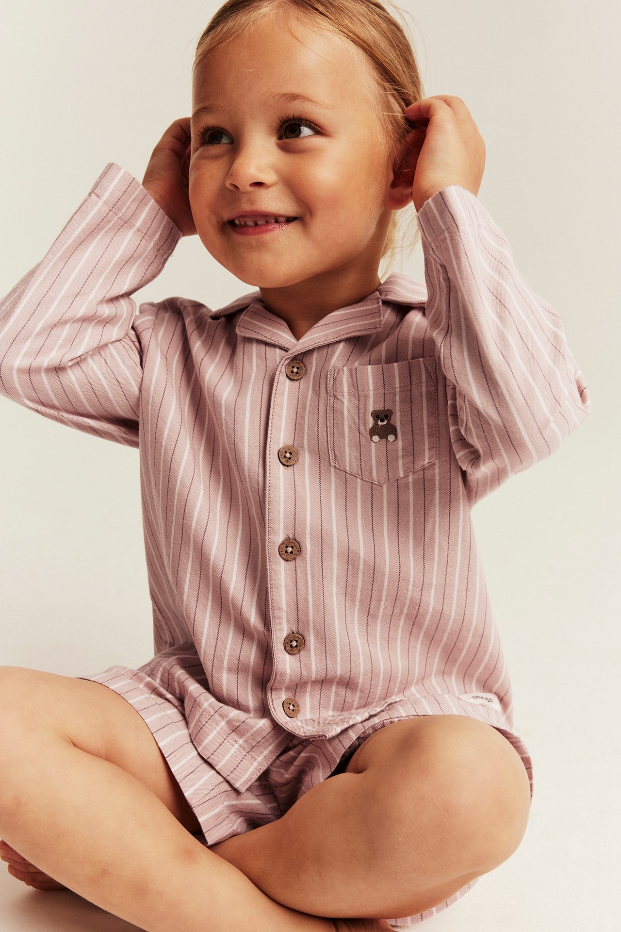 Front view of dusty pink striped pajamas on a kid: long-sleeved top with buttons and matching shorts.