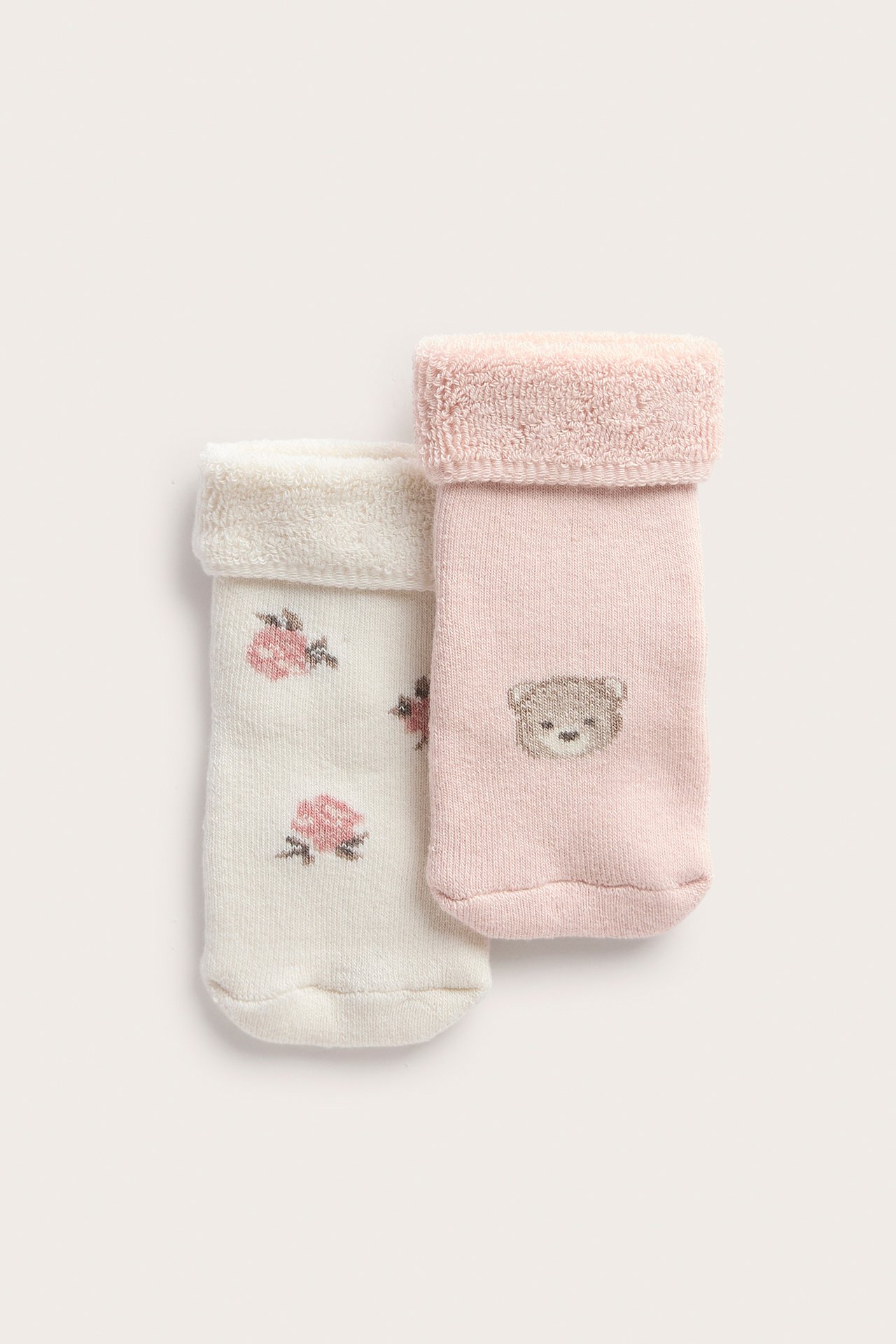 Nahaufnahme von Babysocken; eine rosa mit Teddybär, eine cremeweiß mit Rosen.