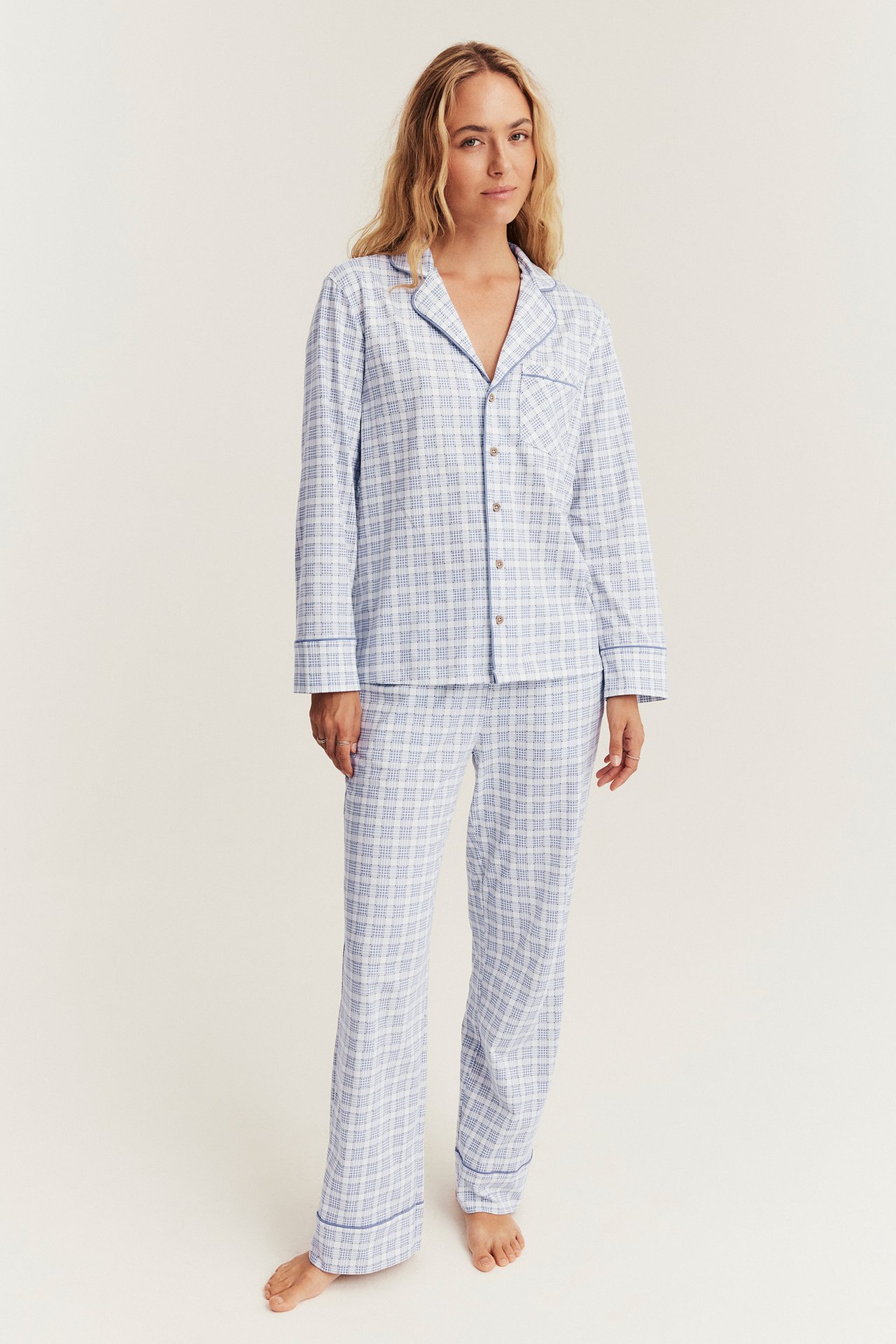 Vorderansicht einer Frau in einem blau-weiß karierten Pyjama-Set mit Hemd und langer Hose.