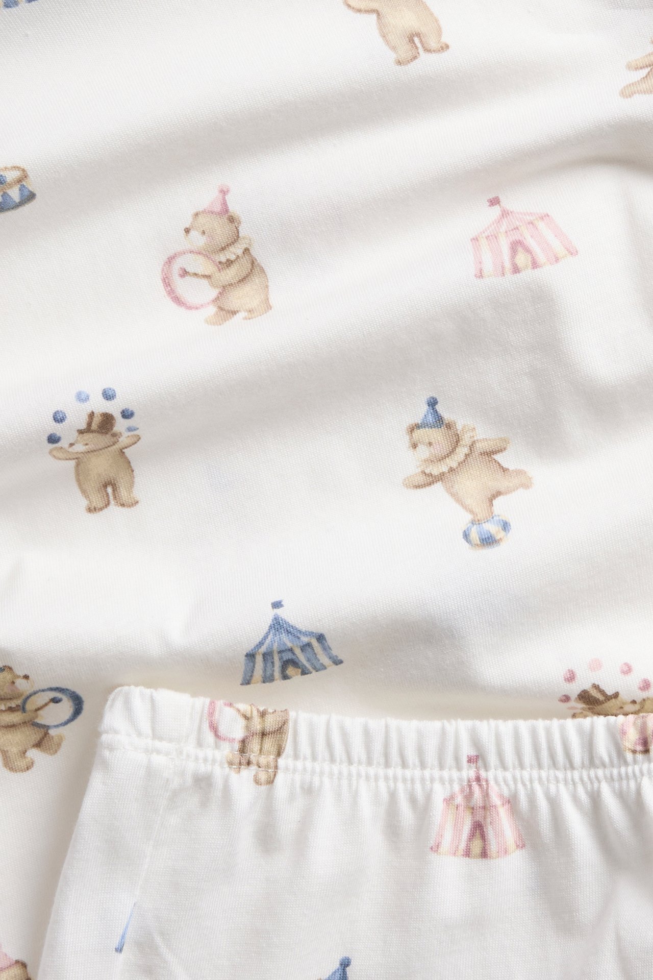 Nahaufnahme eines weißen Baumwoll-Pyjama-Sets mit Pastell-Zirkusbär- und Zelt-Allover-Print.