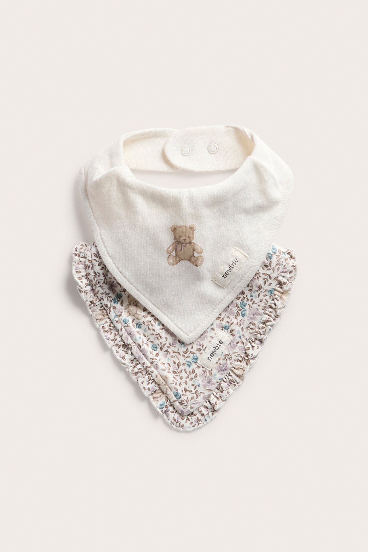 Vorderansicht: Cremefarbenes Baby-Bandana-Lätzchen mit Teddybär und ein florales Babylätzchen.