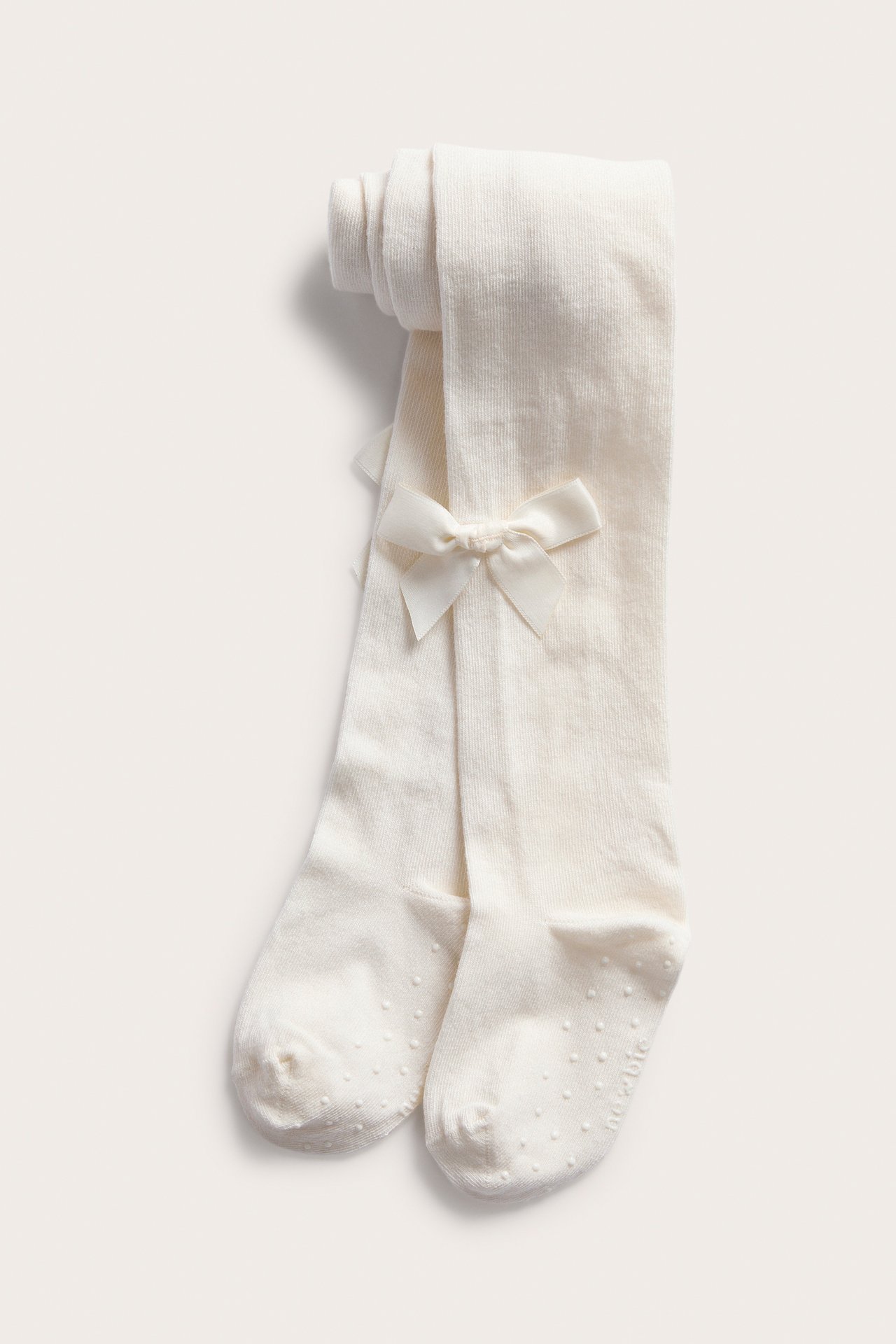 Flat lay of cream ribbed baby tights with bows and anti-slip soles.